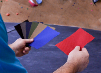 A man looks through nylon fabric swatches in front of a rock climbing wall