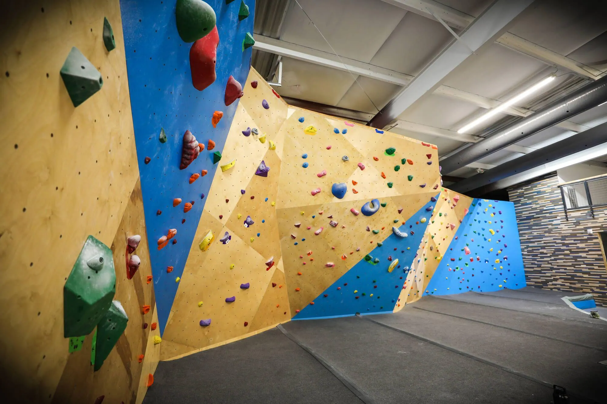 Another view of the North bouldering wall, this time a close-up showing the details involved in the seamless MLM geometric design. The branding extends from the climbing walls to the party room walls, which feature custom-stained hardwood strips.