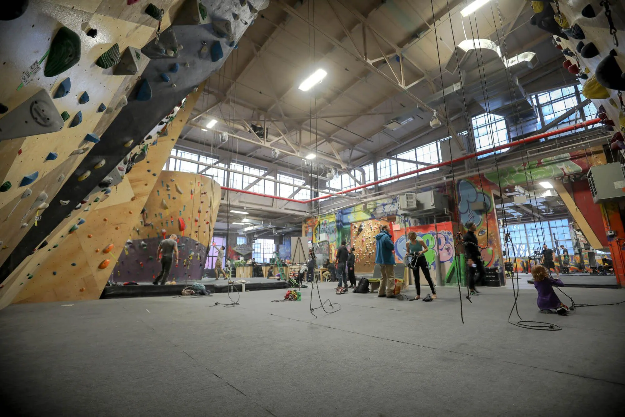 A wide angle view from the dihedral built into the route climbing area, showing the bouldering areas on the left and right, as well as the front desk, strength-training and cardio workout areas.