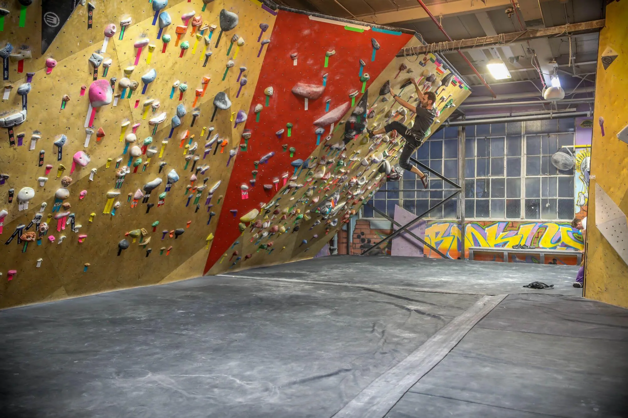Another view of the multi-angle MLM climbing wall area that is completely guarded by the Habit bouldering flooring system. BKB was keen to incorporate a tasteful amount of custom wood stains and paints in their climbing wall designs to match the colorful artwork on all of their interior walls.