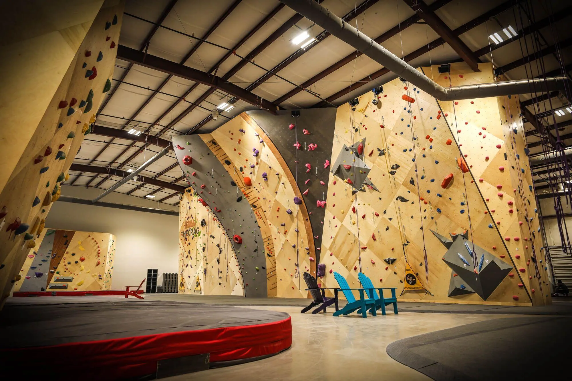 A view next to the big MLM boulder, looking at the complex designs incorporated into the tall route walls. This extra large standalone section features a mixture of ARC and MLM designs and construction, as well as hardwood features with paints matching the gym's brand identity.